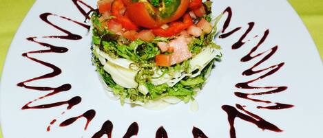 A square plate with a layered salad on a green tablecloth.