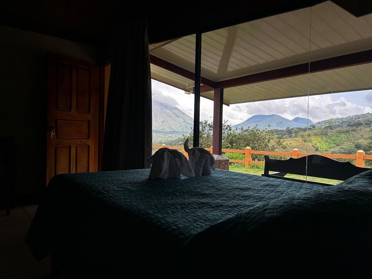 A bedroom with a bed, a wooden door, and a view of mountains through an open window.