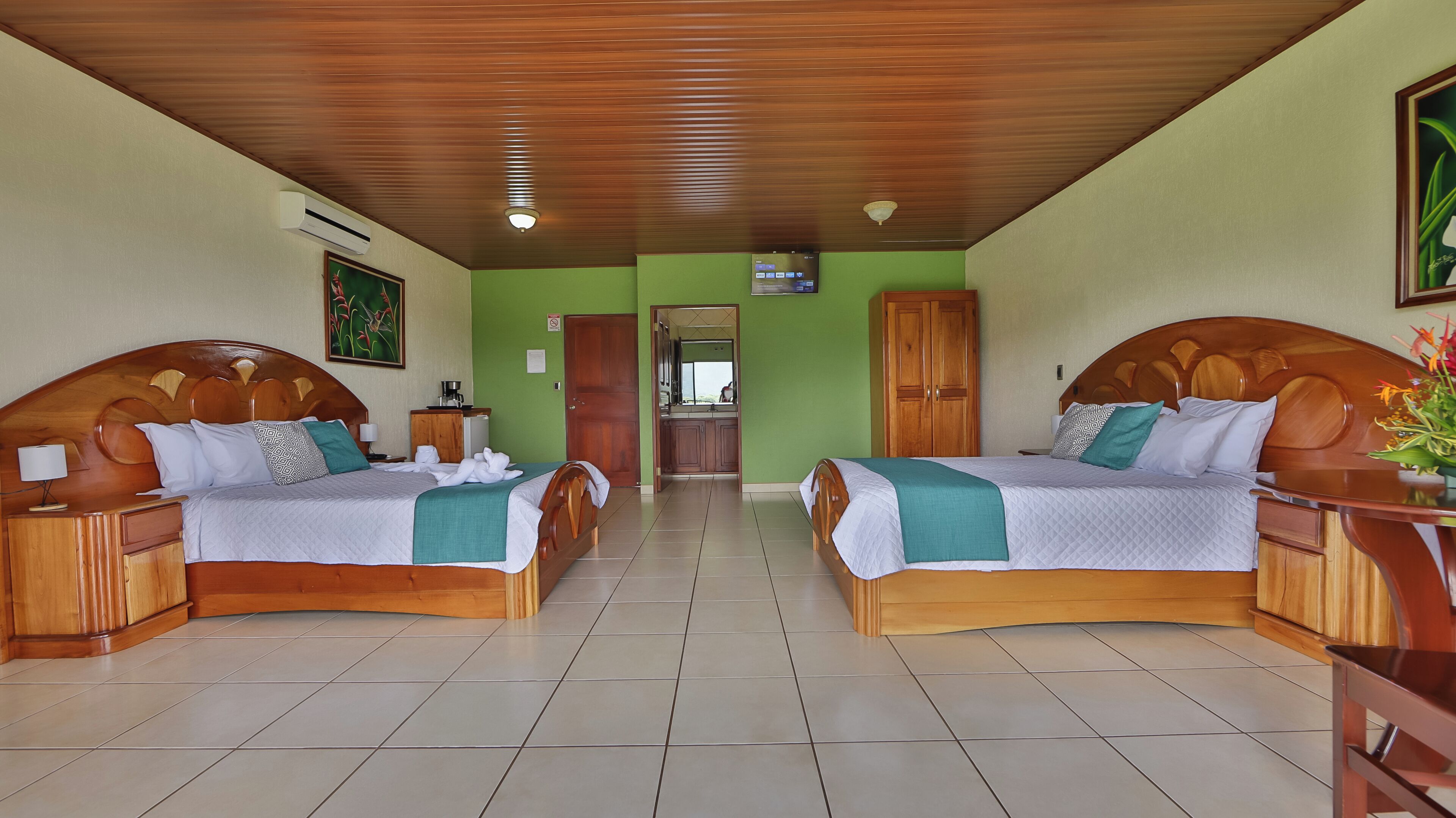 Une chambre d’hôtel avec deux lits en bois, une petite kitchenette et une salle de bain visible à travers une porte ouverte.