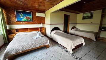 A bedroom with a large bed, two smaller beds, wooden ceiling, tiled floor, and artwork on the walls.