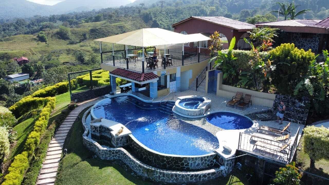 A pool area with a hot tub, lounge chairs, and a covered seating area overlooking a lush landscape.