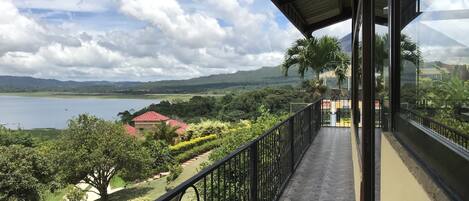 A balcony with a view of a lake, mountains, and a red-roofed building.