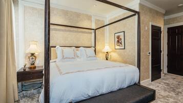 A four-poster bed with a bench, bedside lamps, and a framed artwork on the wall.