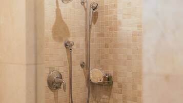 A shower with a handheld showerhead, a wall-mounted faucet, and a shelf with toiletries.