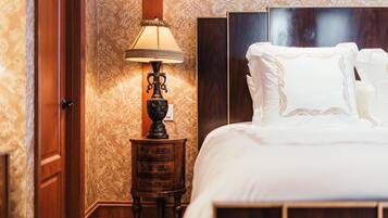 A neatly made bed with white linens and a wooden headboard, a small wooden nightstand with a lamp, and a door with a wooden frame.