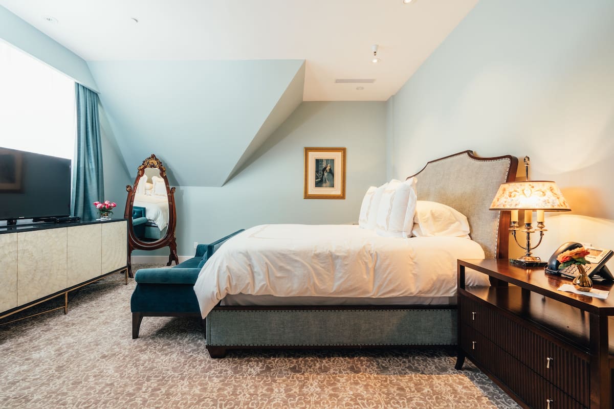 A bedroom with a bed, a dresser, a mirror, a lamp, and a television.