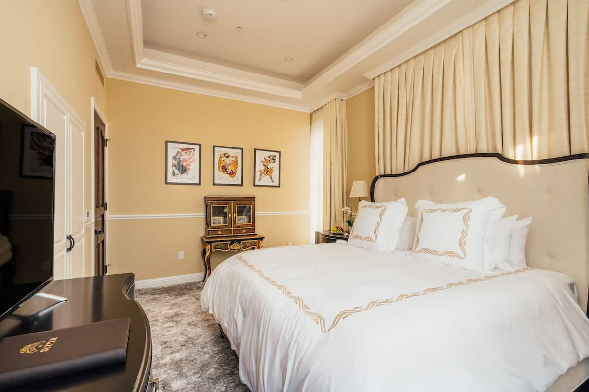 A hotel room with a large bed, a wooden nightstand, a desk, and a mirror. There are three framed pictures on the wall.
