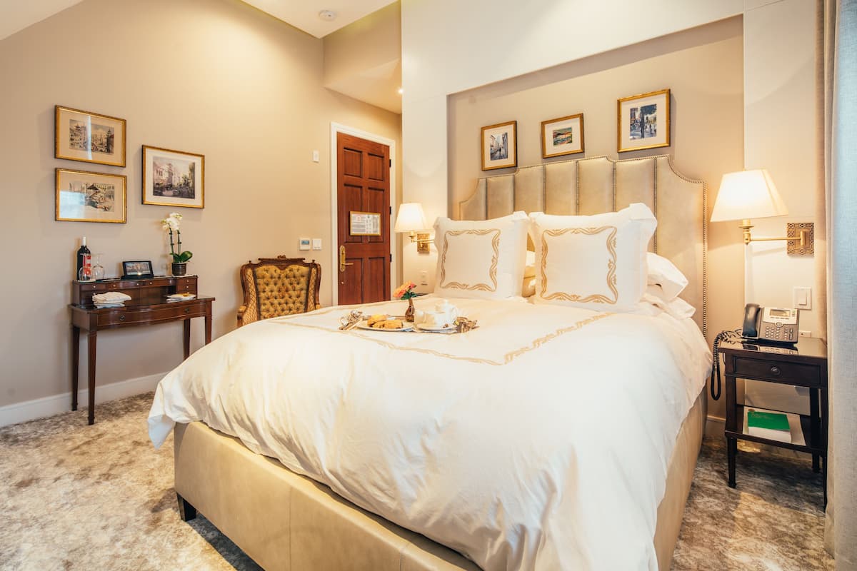 A well-appointed hotel room with a large bed, a wooden nightstand, a desk, and a chair.