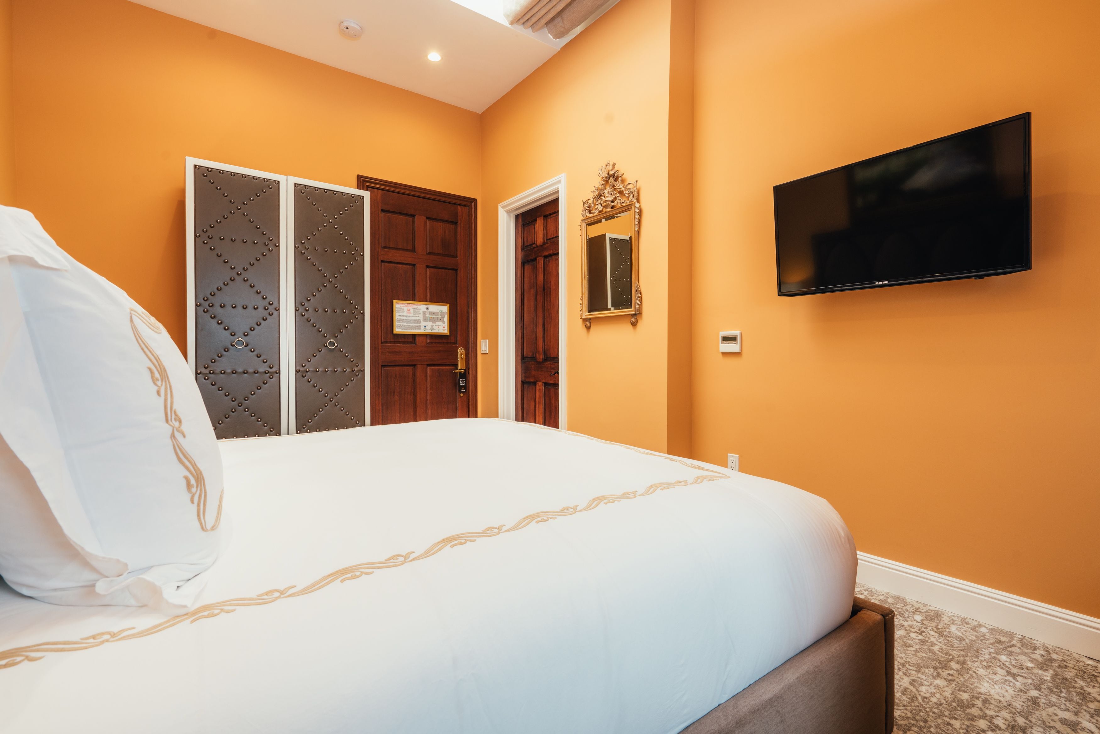 A hotel room with a large bed, a television mounted on the wall, and a door with a decorative mirror.