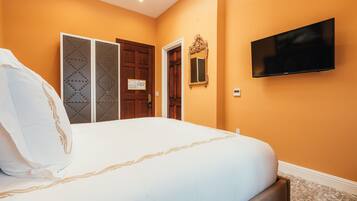 A hotel room with a large bed, a television mounted on the wall, and a door with a decorative mirror.