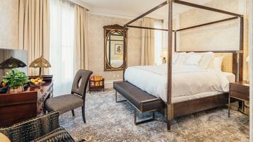 A four-poster bed with a bench, a desk with a lamp, a chair, and a mirror in a hotel room.