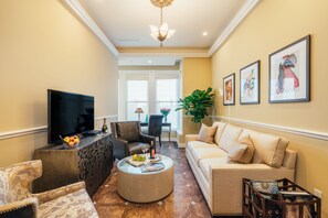 A living room with a flat-screen TV, a round coffee table, a sofa, and a dining area in the background. - Sutter Mansion (San Francisco)