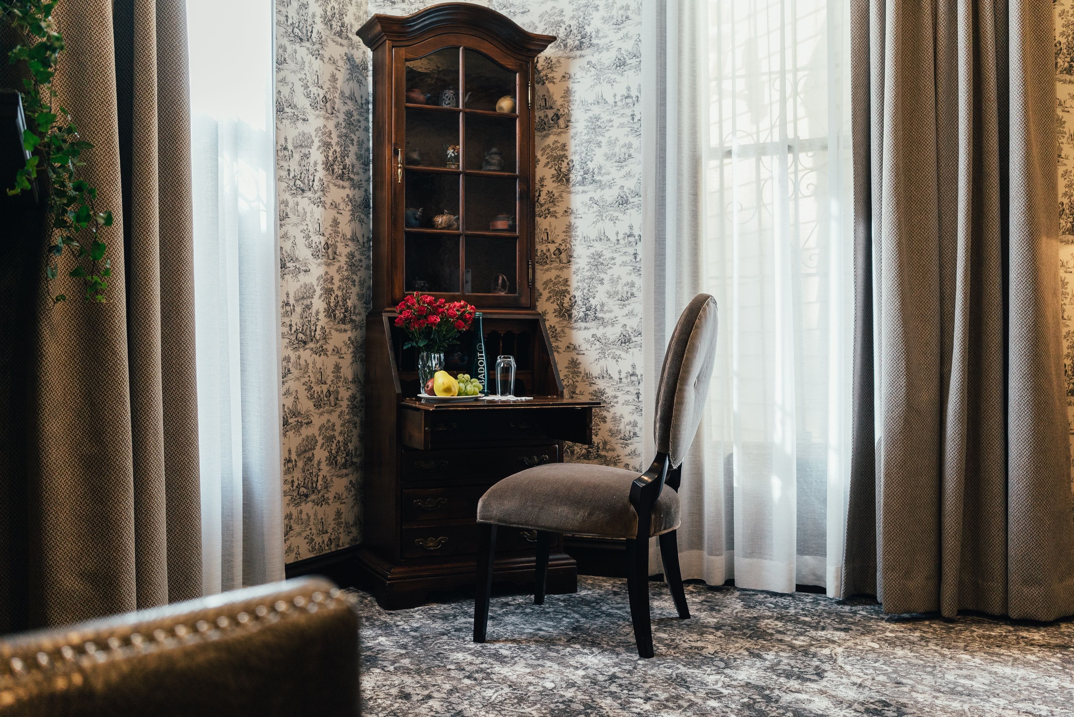 Una habitación con un armario de madera, una silla y un papel tapiz con motivos florales.