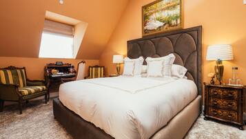 A bedroom with a large bed, a desk, a chair, and a nightstand with a lamp.