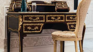 A dark wooden desk with gold accents, a vase with red flowers, and a chair with a floral pattern.