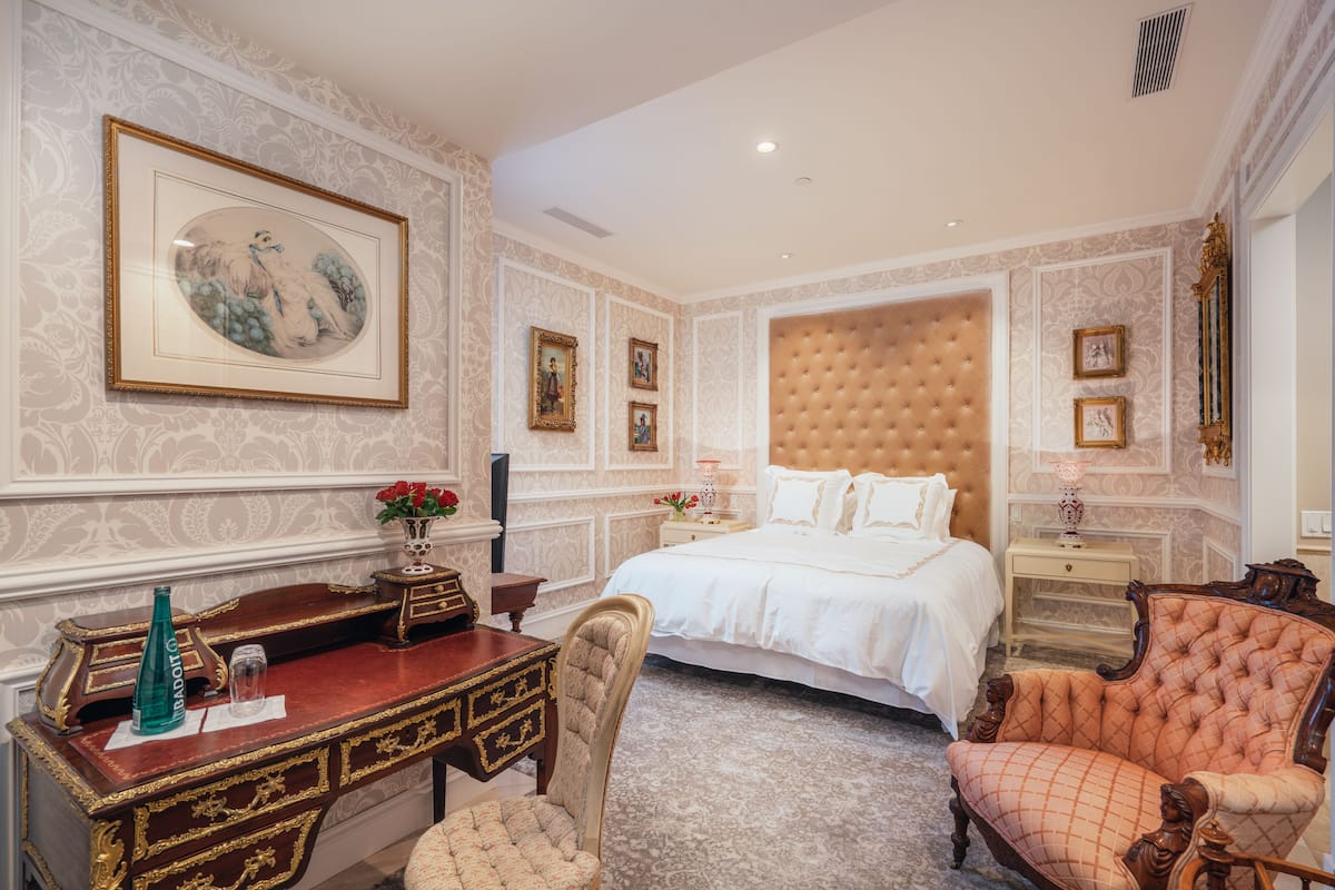 A luxurious bedroom with a large bed, a desk with a chair, and a decorative chair.
