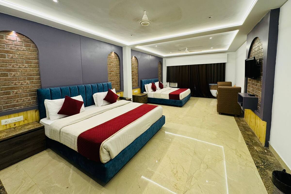 A modern hotel room with two beds, a flat-screen TV, and a fireplace.