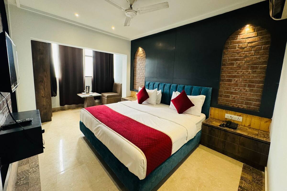 A hotel room with a large bed, a desk, a chair, a ceiling fan, and a brick accent wall.