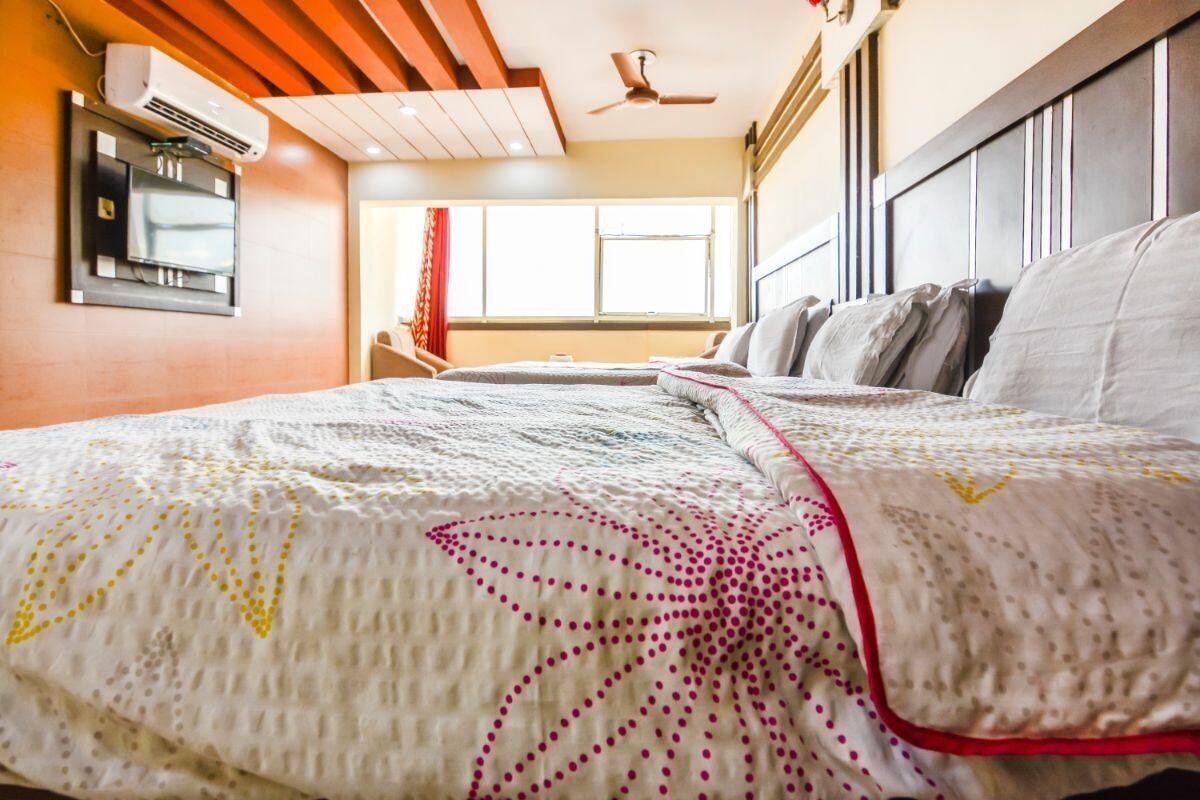 A hotel room with a large bed, a ceiling fan, an air conditioning unit, and a window with curtains.