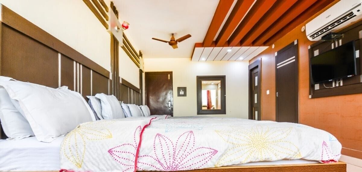 Een hotelkamer met een groot bed, een plafondventilator, een airconditioning en een aan de muur bevestigde televisie.