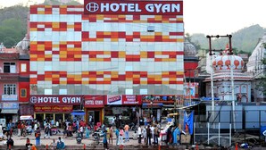 A hotel with a large sign, a busy street in front, and a temple nearby. - Hotel Gyan (Haridwar)