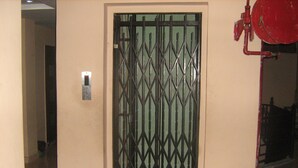 A door with a metal gate, a wall-mounted light switch, and a red fire hydrant. - Hotel Gyan (Haridwar)