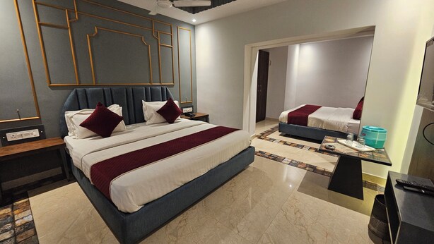 A hotel room with a large bed, a smaller bed, a desk with a computer, and a water dispenser. - Hotel Gyan (Haridwar)