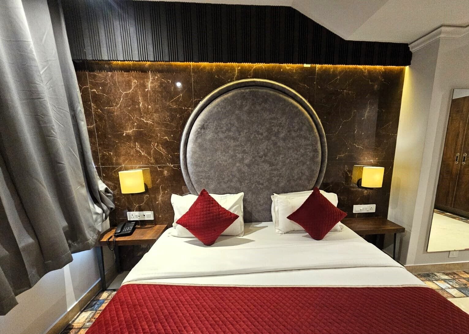 Une chambre d’hôtel avec un grand lit, un mur en marbre, deux lampes de chevet et une couvre-lit rouge matelassée.