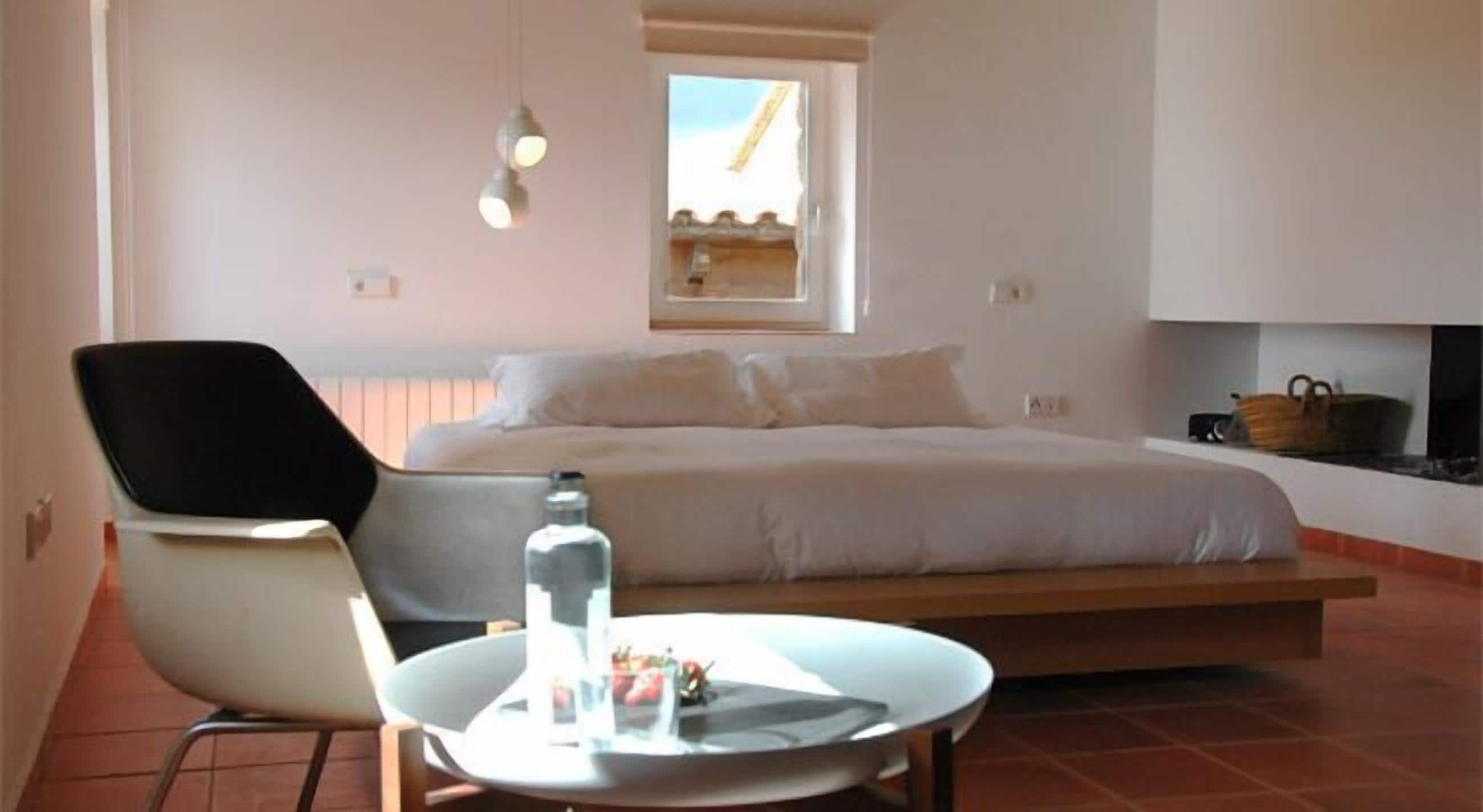 Un dormitorio con cama, una silla, una mesa y un ventanal.