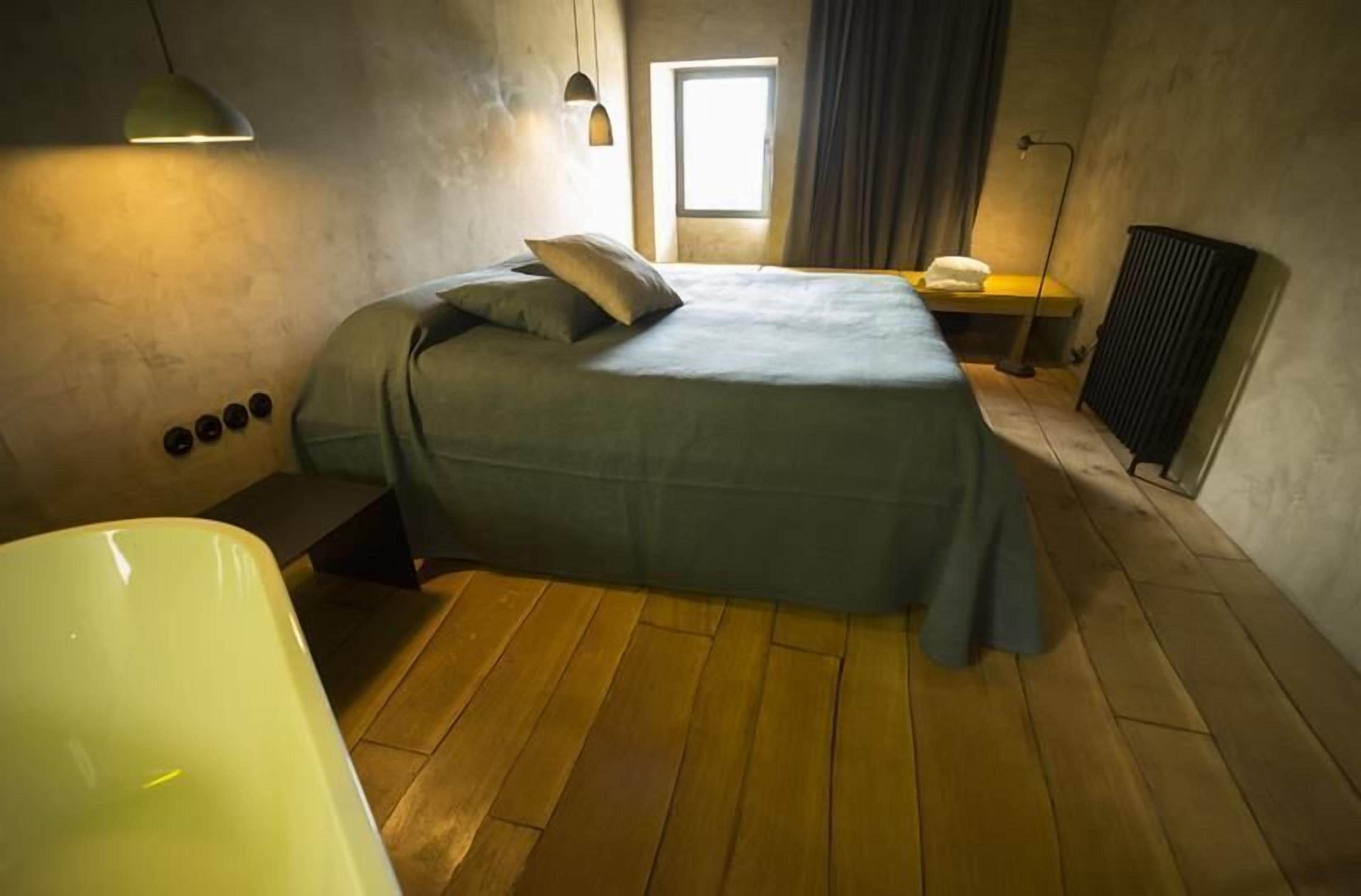 A bedroom with a bed, a window, a radiator, and a bathtub.