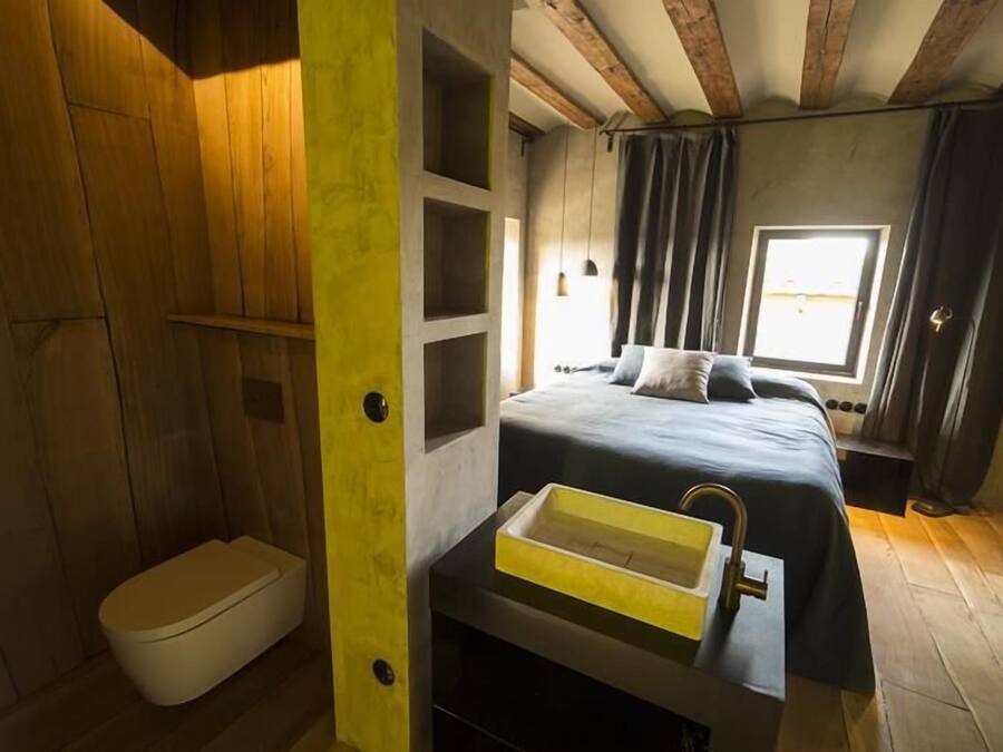 Un dormitorio con cama, ventana, estante empotrado y un baño pequeño con inodoro.