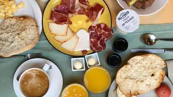 Ein Frühstückstisch mit Brot, Eiern, Schinken, Käse und einer Kaffeetasse.