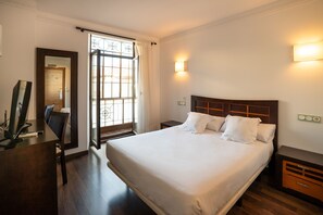 Una habitación de hotel con una cama grande, un escritorio, una silla, una mesita de noche y una ventana con cortinas.