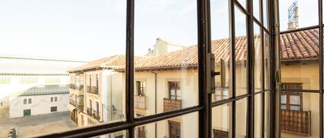 A view through a window of a building with a tiled roof, balconies, and a street below.