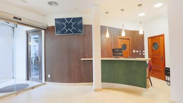Un área de recepción con un mostrador de madera, una alfombra verde y un televisor montado en la pared.