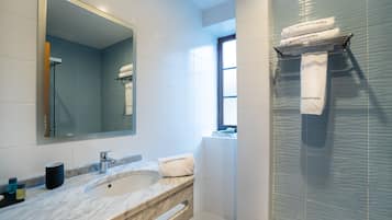 A modern bathroom with a marble sink, a large mirror, and a glass shower enclosure.
