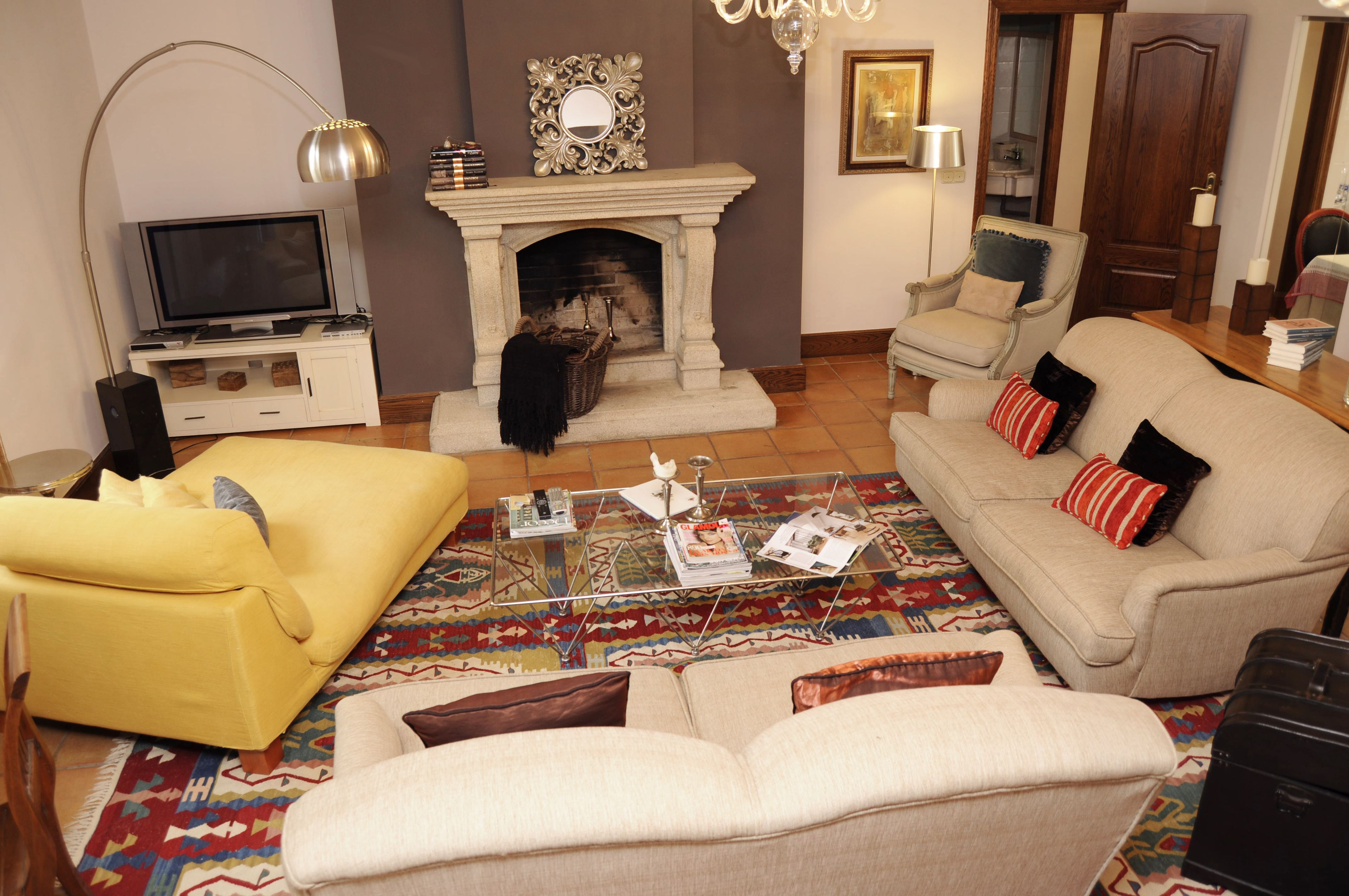 A living room with a fireplace, a yellow sofa, a beige sofa, and a coffee table with magazines.