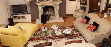 A living room with a fireplace, a yellow sofa, a beige sofa, and a coffee table with magazines.