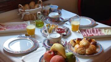 A breakfast table with plates of fruits, croissants, ham, and juice.