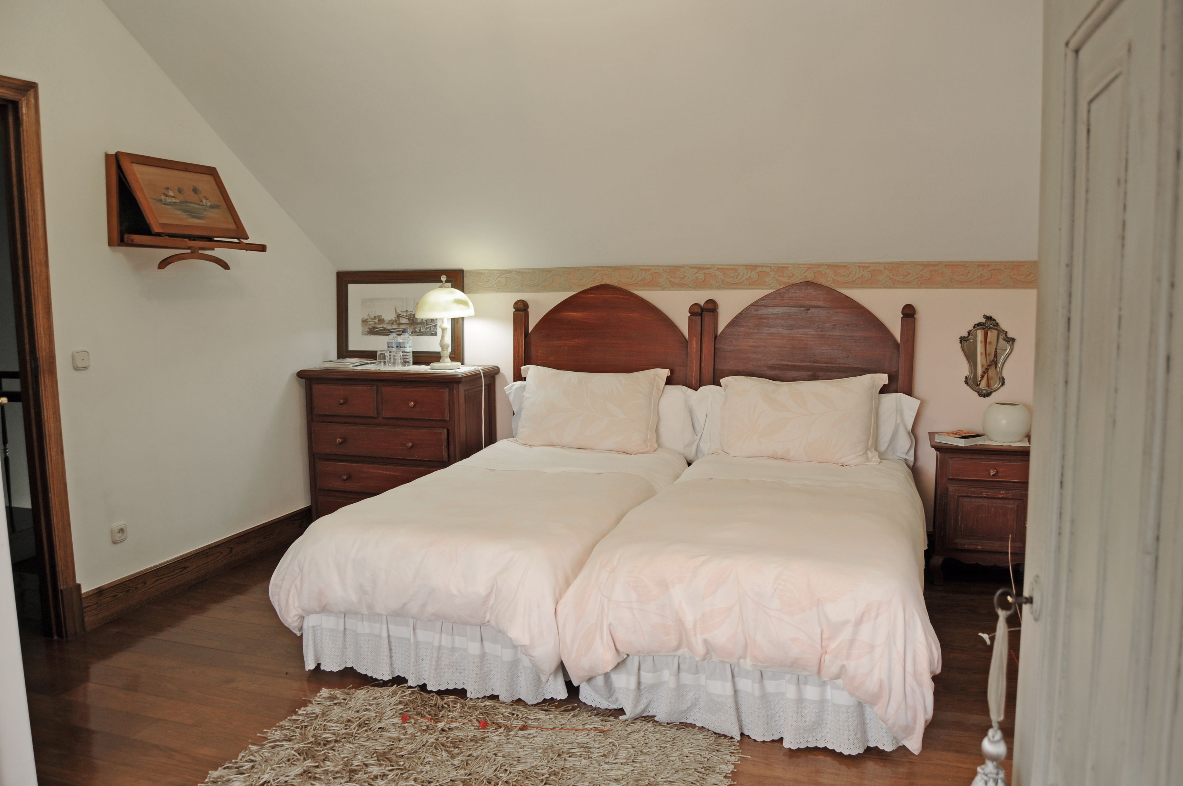 A double bed with a wooden headboard, a bedside table with a lamp, and a small dresser.