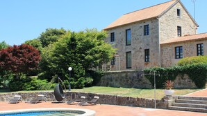 Un edificio de piedra con piscina, mobiliario de exterior y un jardín bien cuidado.