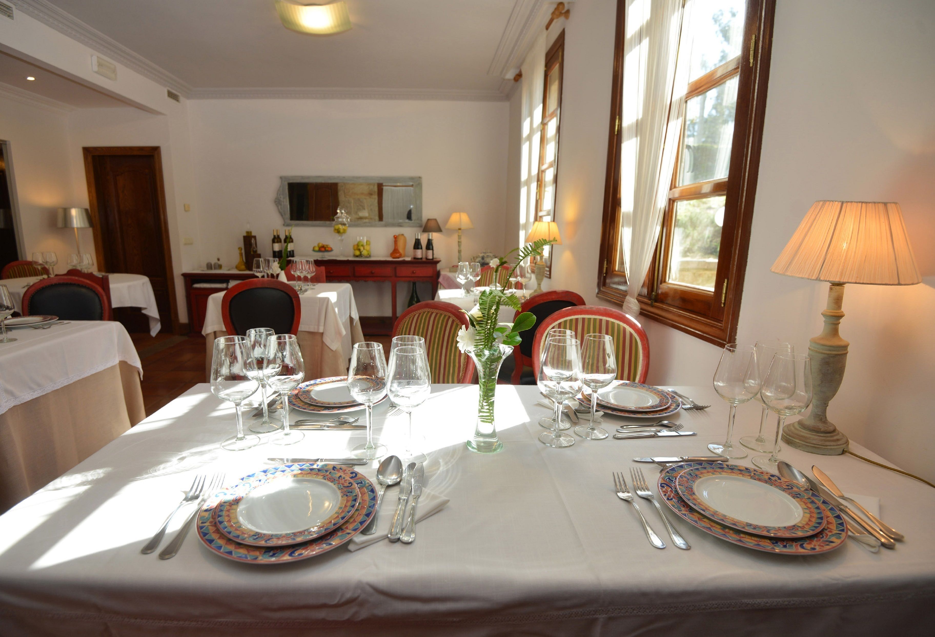 Comedor con mesas dispuestas para cuatro, cada una con platos, cubiertos y copas de vino.