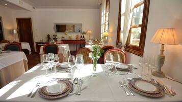 Comedor con mesas dispuestas para cuatro, cada una con platos, cubiertos y copas de vino.