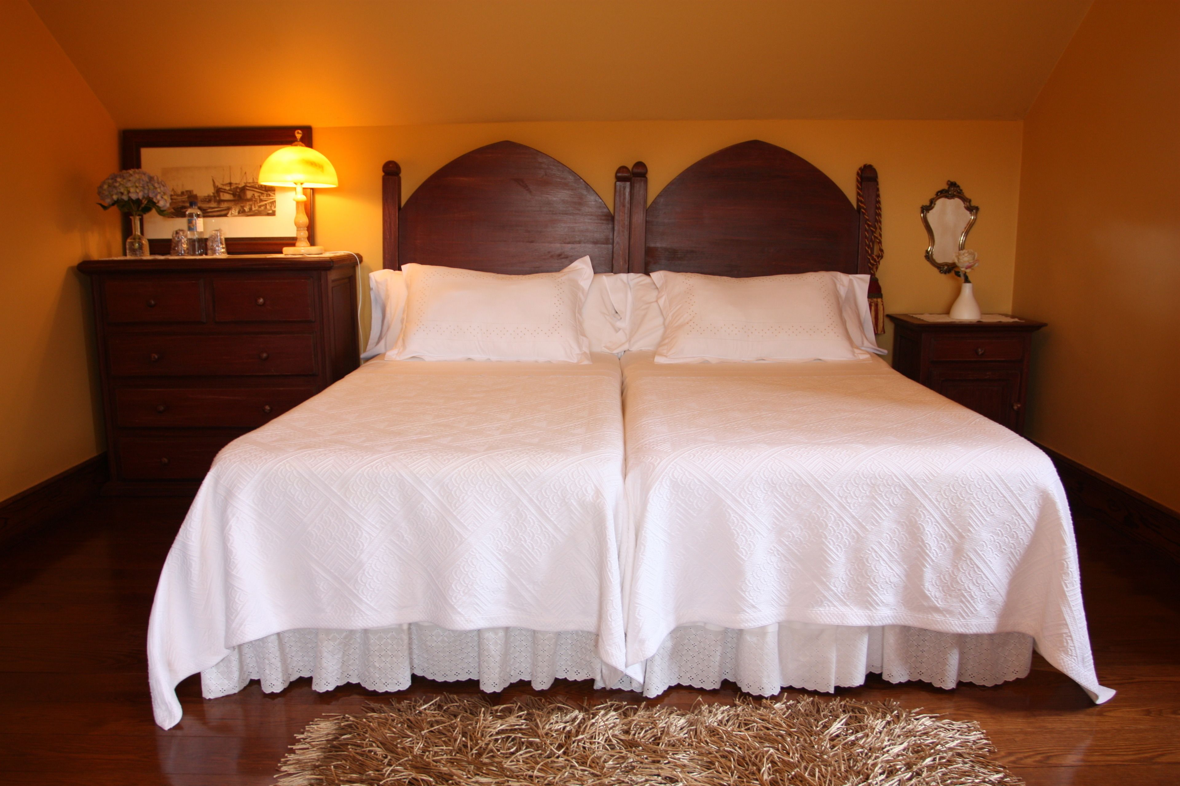 Una cama doble con cabecera de madera, una mesita de noche con lámpara y un espejo en la pared.