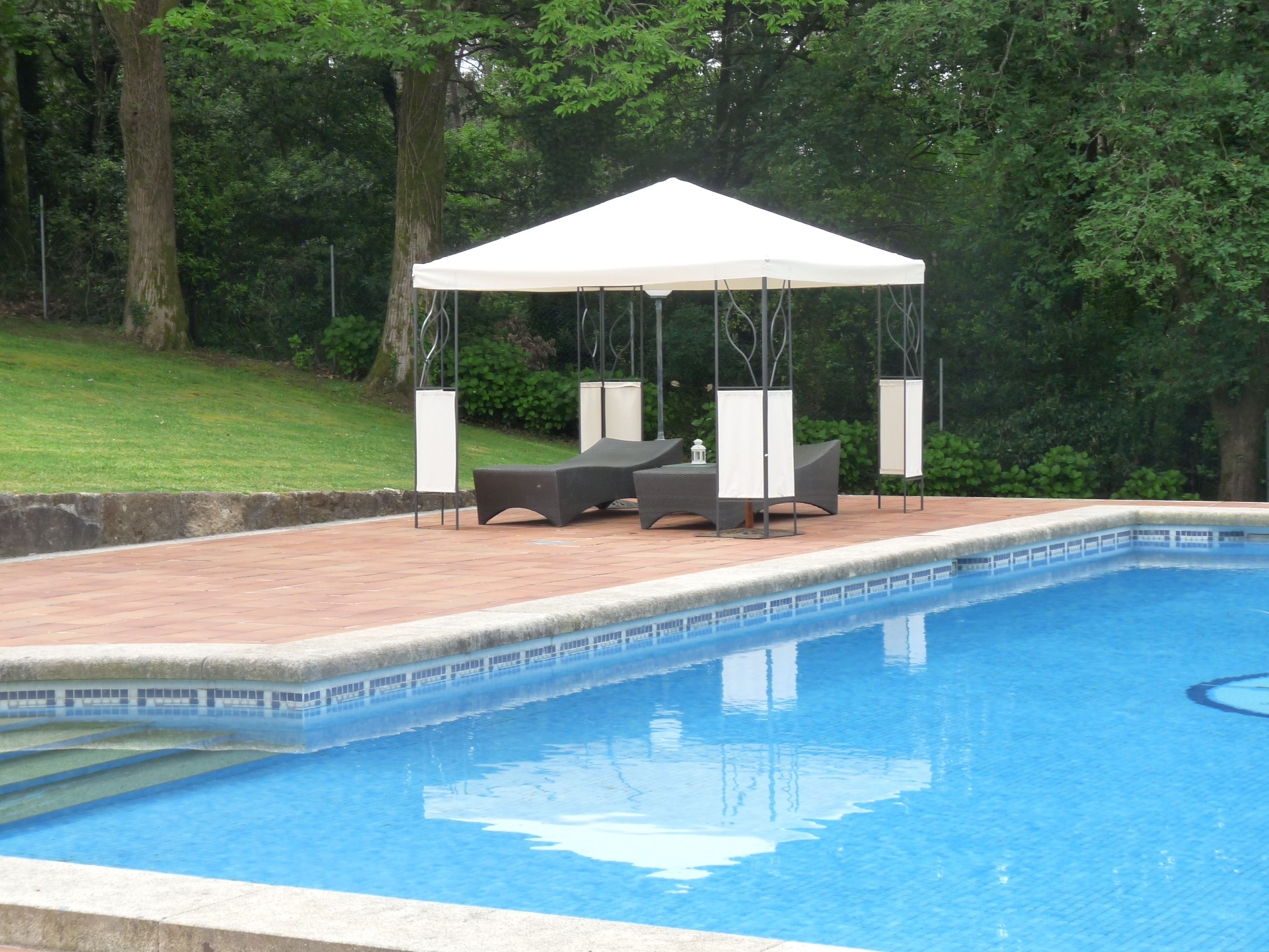 A swimming pool with a covered seating area and lounge chairs.