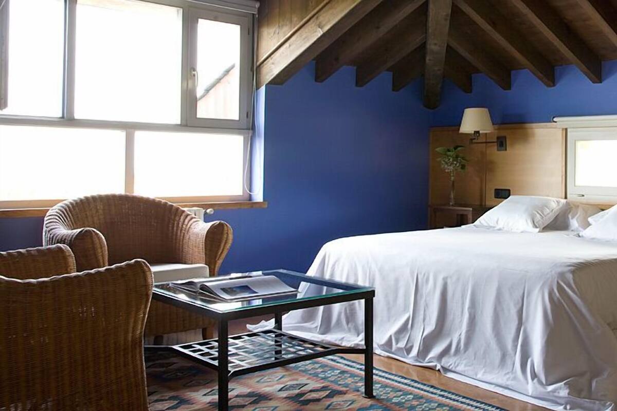 Een slaapkamer met een bed, twee nachtkastjes, een stoel, een tafeltje en een raam.