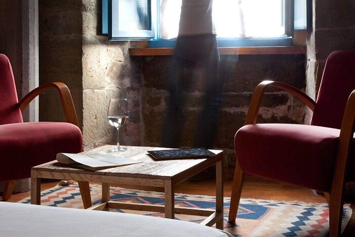 Een kamer met twee rode fauteuils, een houten tafel met een glas en een boek, en een kamerbreed tapijt met een patroon.