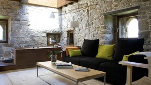 A stone-walled room with a wooden bench, a sofa with green cushions, and a coffee table with books and a vase of flowers. - Rusticae Hotel Torre de Villademoros (Valdes)