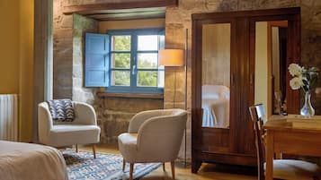 Una habitación con cama, dos sillas, un armario de madera, una ventana con contraventanas azules y una alfombra estampada.