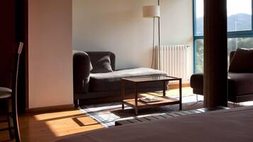 Habitación de hotel con cama, una mesita, un sofá, una lámpara de pie y vistas al exterior.